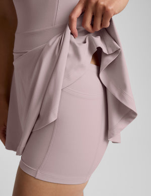 Woman wearing a pink mini pleated athletic dress against a plain background. 