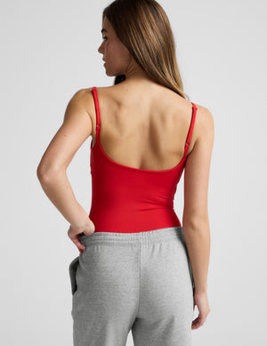 Woman wearing a red bodysuit and gray sweatpants against a plain background. 