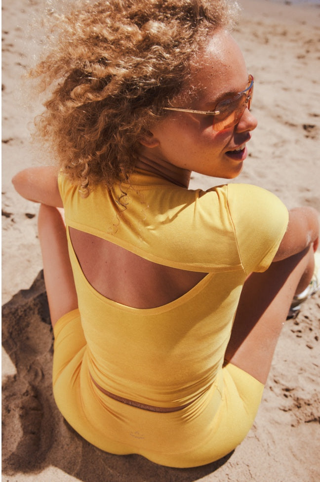 model is wearing a yellow cropped t-shirt with a key hole detail in the back. 