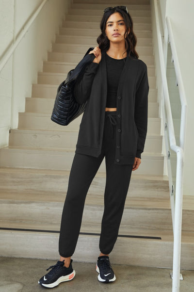 model is wearing a black button up cardigan and black high-waisted midi joggers. 