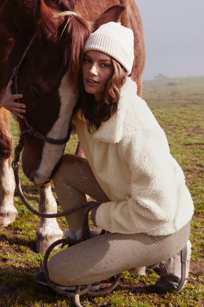 model is wearing a white quarter zip faux sherpa pullover and beige star printed high-waisted midi leggings. 