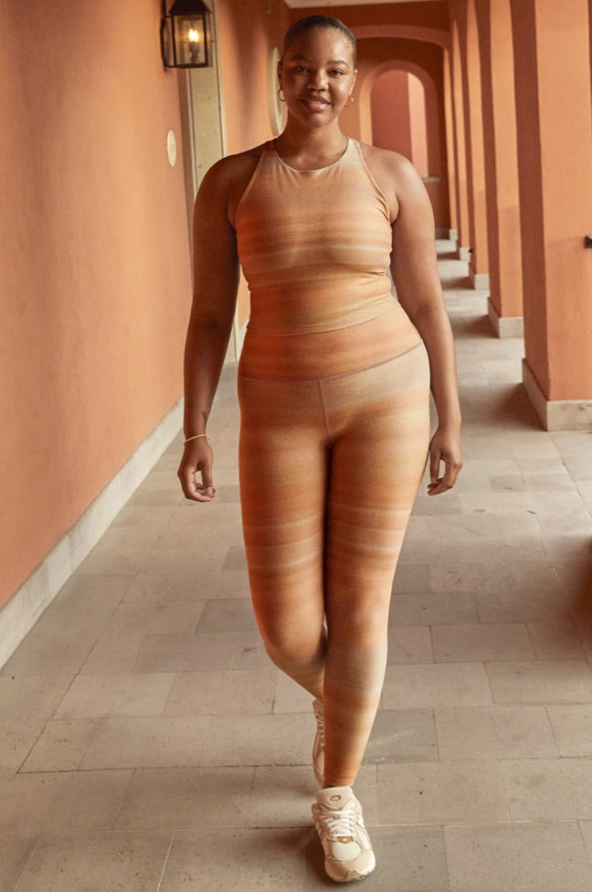 model is wearing an orange ombre striped high-neck racerback cropped tank and orange ombre striped high-waisted midi leggings. 