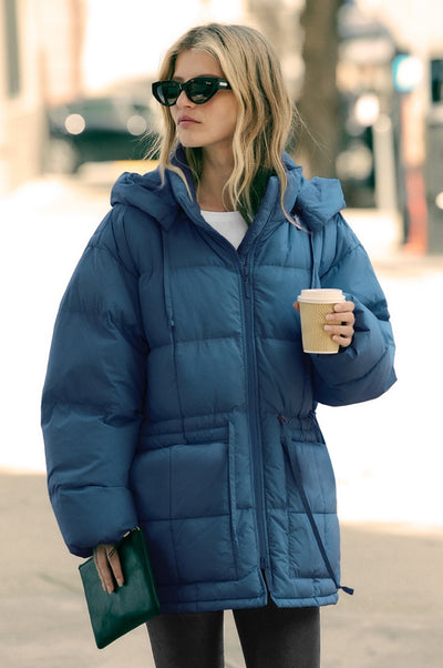 model is wearing a blue zip-up puffer jacket. 