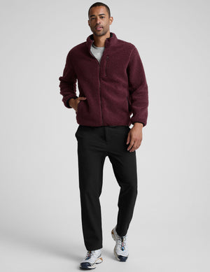 model wearing a burgundy fleece men's zip-up jacket on a gray background. 