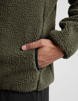 model wearing a men's green fleece zip-up jacket on a light gray background. 