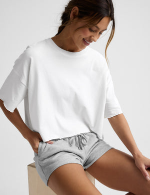 Woman wearing a white cropped t-shirt and gray fleece shorts against a plain background. 