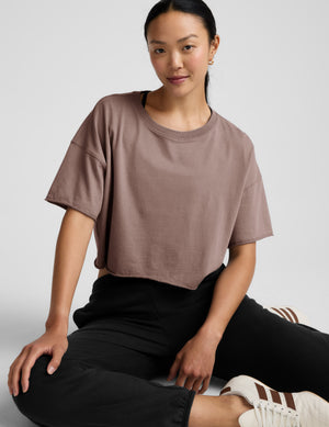 Woman wearing a brown cropped top and black pants on a light gray background. 