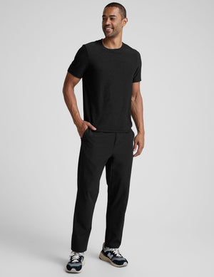 Man wearing a black t-shirt and black pants on a light gray background. 