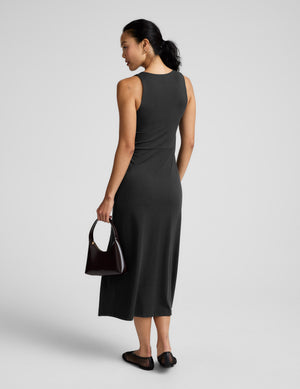 Woman wearing a black square neck midi length dress against a plain background. 