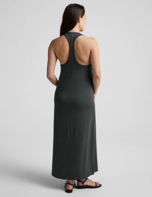 Woman wearing a dark green sleeveless dress on a light gray background. 