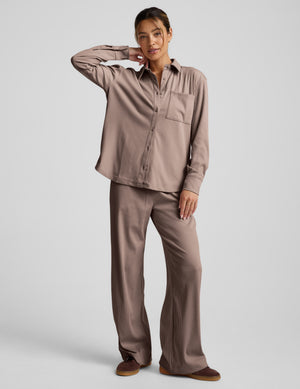 Woman wearing a brown corduroy button-up shirt and pants on a light gray background. 