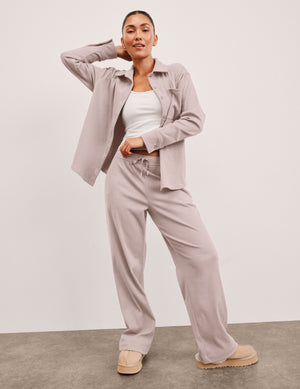 Woman wearing a pink corduroy button up shirt and pants against a plain background. 