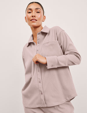 Woman wearing a pink corduroy button up shirt and pants against a plain background. 