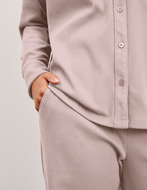Woman wearing a pink corduroy button up shirt and pants against a plain background. 