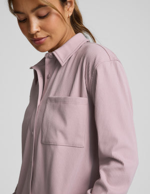 Woman wearing a pink corduroy button down shirt and pants against a plain background. 