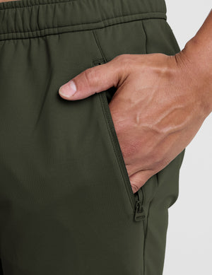 close-up of a hand inserting into a pocket of green pants on a white background. 