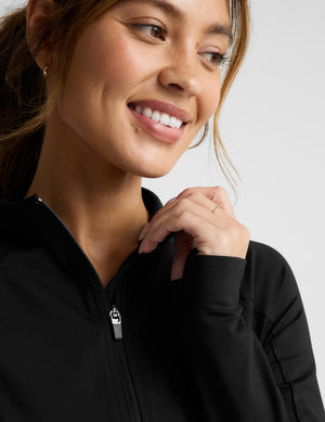 Woman wearing a black jacket on a light gray background. 