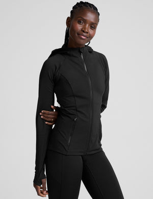 woman in black zip-up hooded jacket and leggings against a plain background. 
