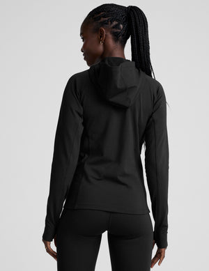 woman in black zip-up hooded jacket and leggings against a plain background. 