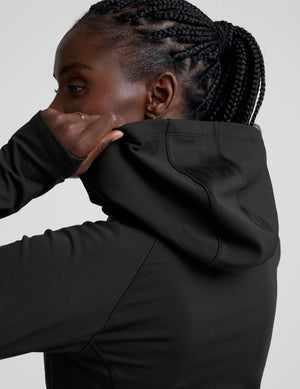 woman in black zip-up hooded jacket and leggings against a plain background. 