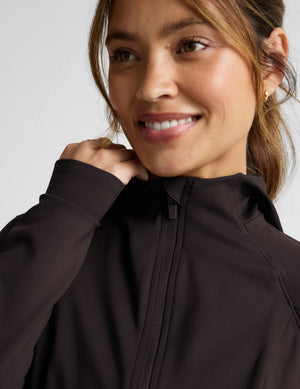 Woman wearing a brown jacket and leggings on a light gray background. 