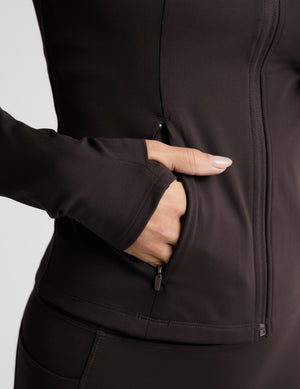 Woman wearing a brown jacket and leggings on a light gray background. 