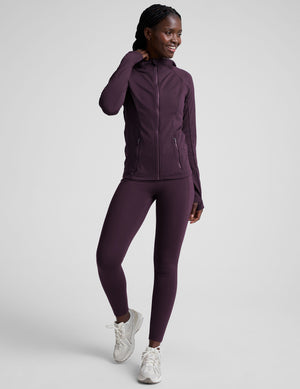 woman wearing a purple hooded jacket and leggings on a plain background. 