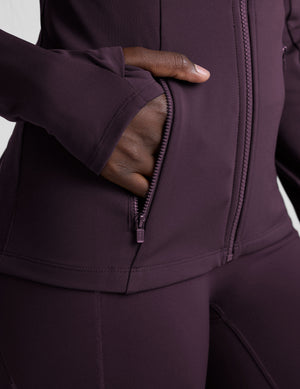 woman wearing a purple hooded jacket and leggings on a plain background. 