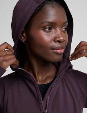 woman wearing a purple hooded jacket and leggings on a plain background. 