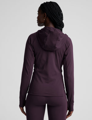 woman wearing a purple hooded jacket and leggings on a plain background. 