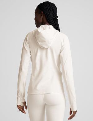 woman wearing a white athletic hooded jacket and leggings on a plain background. 