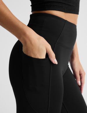 Woman wearing a black quarter zip and leggings on a light gray background. 