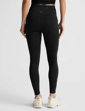 Woman wearing a black quarter zip and leggings on a light gray background. 