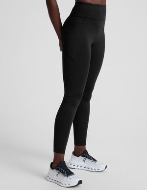 woman wearing a black high-waisted long length leggings with pockets athletic outfit on a plain background. 