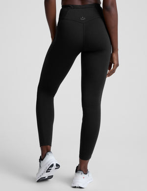 woman wearing a black high-waisted long length leggings with pockets athletic outfit on a plain background. 