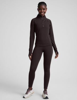 person wearing brown high-waisted long leggings with pockets on a plain background. 