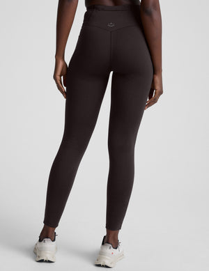 person wearing brown high-waisted long leggings with pockets on a plain background. 
