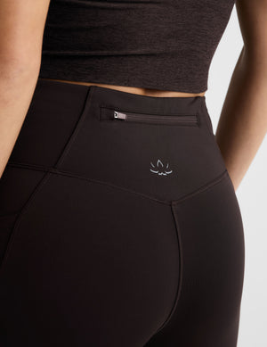 Woman wearing a brown long-sleeve top and leggings on a white background. 