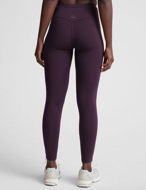 woman wearing high-waisted purple long length leggings with pockets against a plain background. 