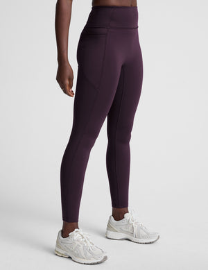 woman wearing high-waisted purple long length leggings with pockets against a plain background. 