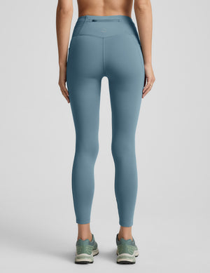 Woman wearing a blue fleece lined blue leggings with pockets on a light gray background. 