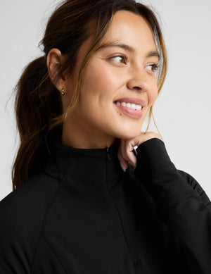Woman wearing a black quarter zip pullover and leggings on a light gray background. 
