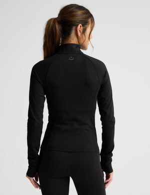 Woman wearing a black quarter zip pullover and leggings on a light gray background. 