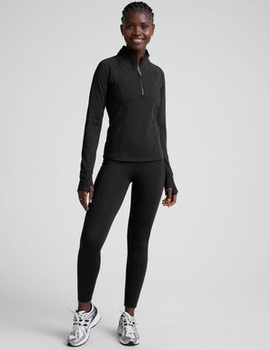 woman wearing a black long-sleeve athletic jacket with a zipper on a plain background. 