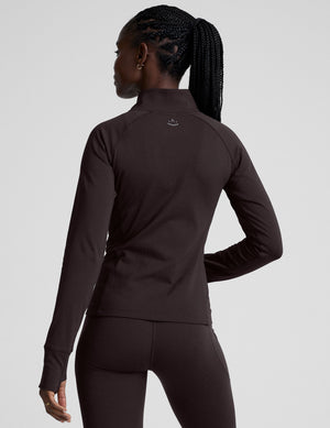 woman wearing a brown quarter-zip jacket and leggings on a plain background. 
