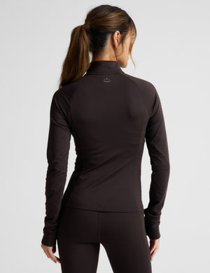 Woman wearing a brown quarter zip pullover and leggings on a light gray background. 