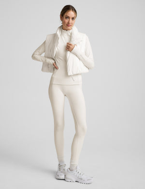 Woman wearing a white quarter zip jacket, white vest, and white leggings against a plain background. 