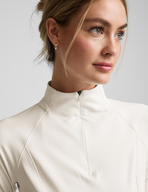 Woman wearing a white quarter zip jacket and white leggings against a plain background. 