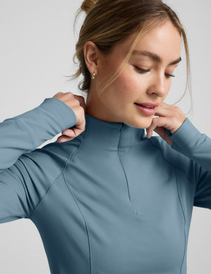 Woman wearing a blue quarter zip pullover and blue leggings on a light gray background. 