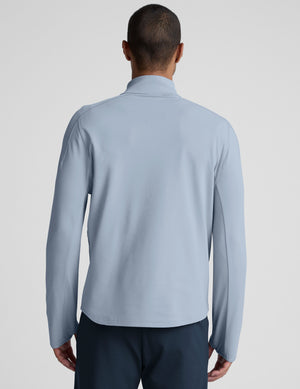 Man wearing a light blue quarter zip pullover and blue pants on a plain background. 